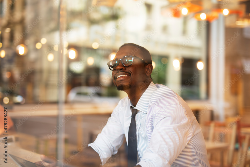 Obraz premium Businessman drinking coffee in cafe. Handsome African man using digital tablet while enjoy in fresh coffee