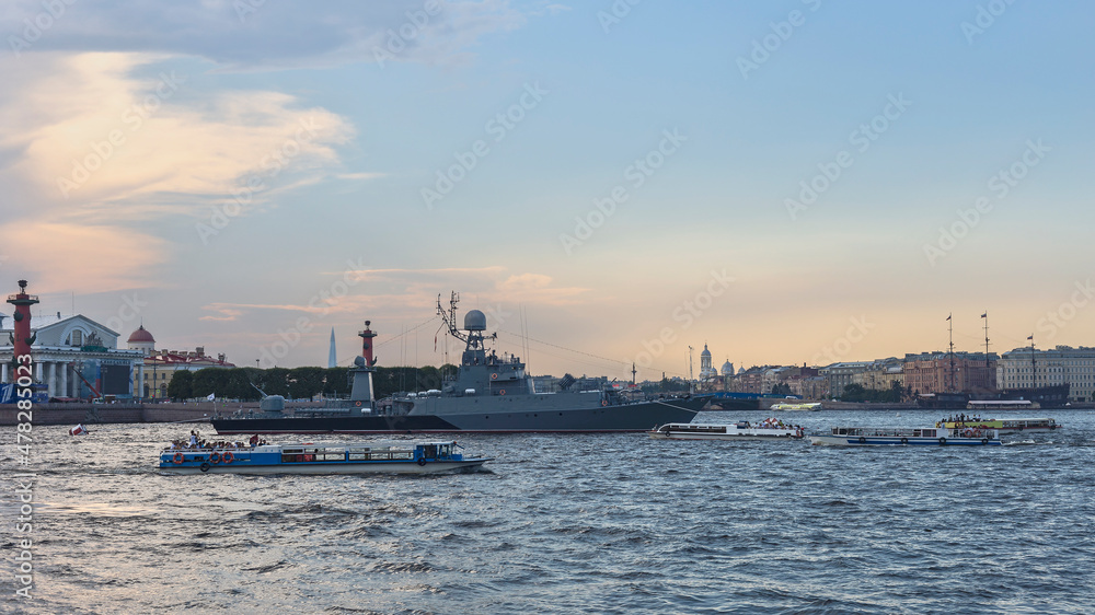 Russian military ship on the Neva in the center of the city surrounded by pleasure boats with tourists against the background of a blue sky