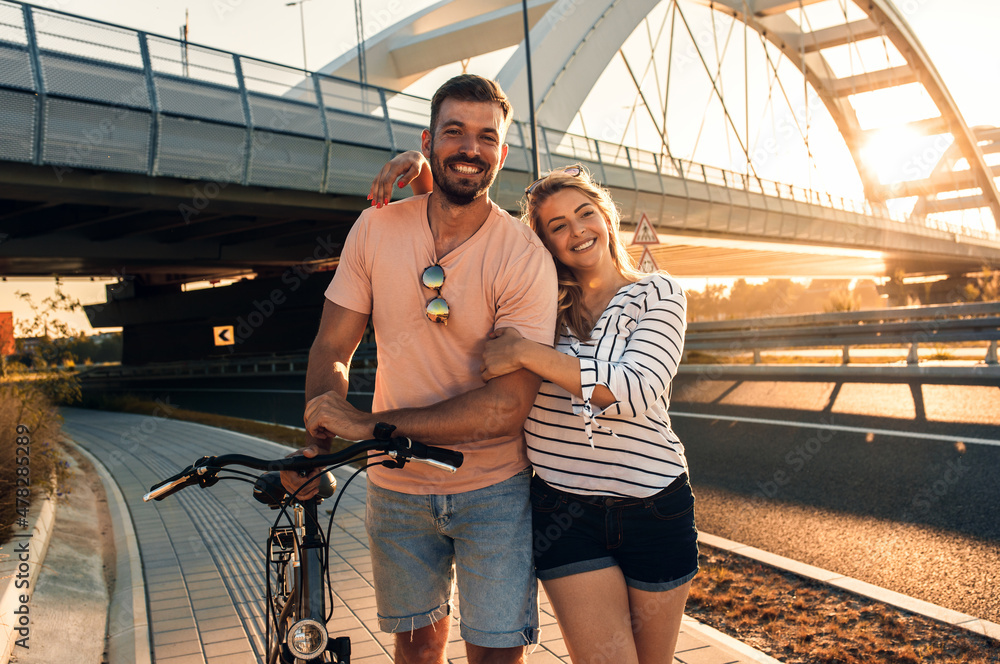Young couple with bicycle enjoying walking and embracing each other at sunset.