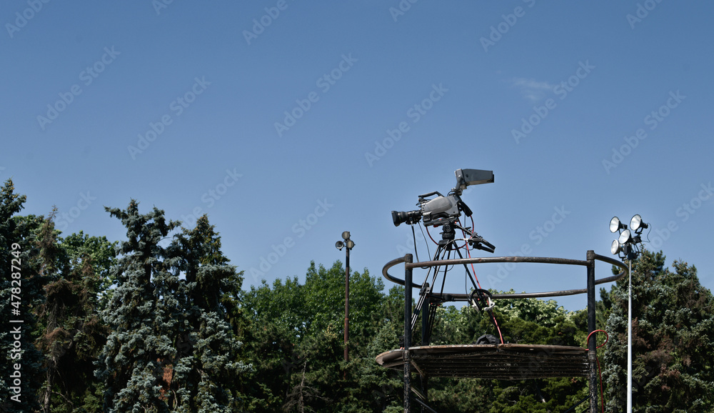 Television broadcast camera system standing on a tripod for a live stand up position with blue sky background. Television broadcast camera system standing on a tripod for a live stand up position with blue sky background.