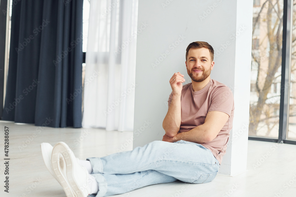 Man in casual clothes is sitting on the floor in modern domestic room