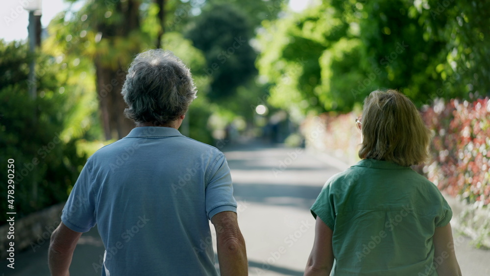 Naklejka premium Romantic senior husband putting arm around wife, back view of older couple walking together in green path
