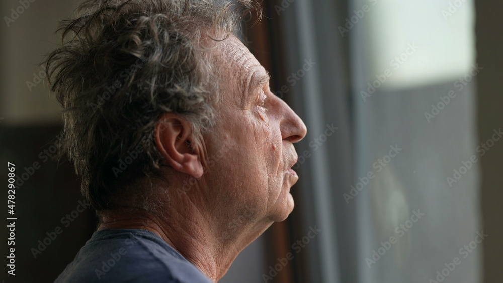 Pensive senior man standing by window looking outside. Thoughtful old person Pensive senior man standing by window looking outside. Thoughtful old person