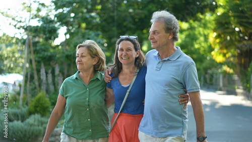 Parents walking with adult daughter together, family day walk outside laughing and smiling
