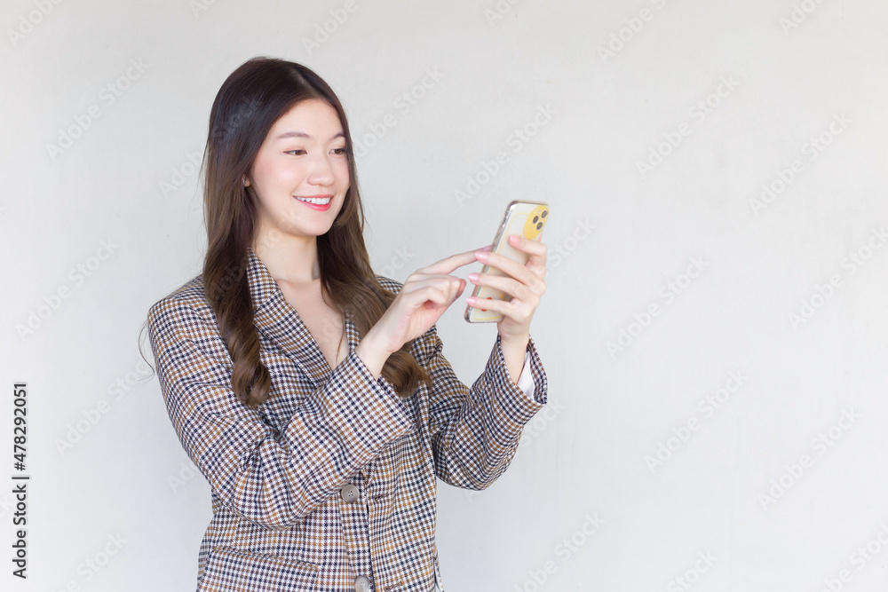 Asian professional woman with black long hair wearing a plaid suit and pretty happily using a smartphone on a white background. Asian professional woman with black long hair wearing a plaid suit and pretty happily using a smartphone on a white background.