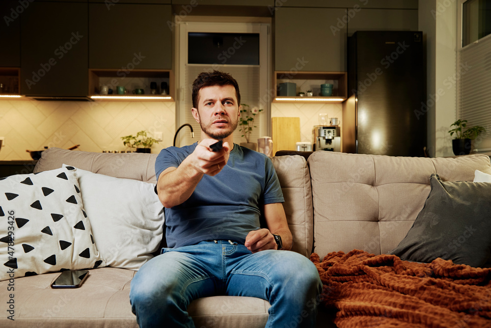 Obraz premium Man watching tv set at lazy weekend, resting at living room, use remote control to switch channels