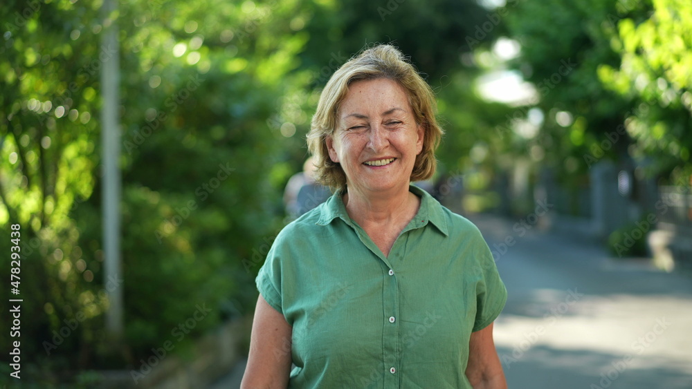 Happy senior woman walking forward smiling in city nature Happy senior woman walking forward smiling in city nature