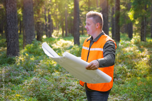 Forest engineer or surveyor holding maps and inspecting forest land photo