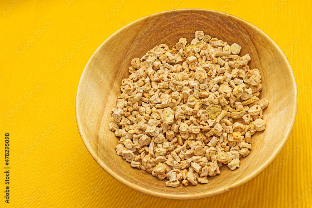 Wooden plate with dried pieces of parsley root on a yellow background close-up Wooden plate with dried pieces of parsley root on a yellow background close-up