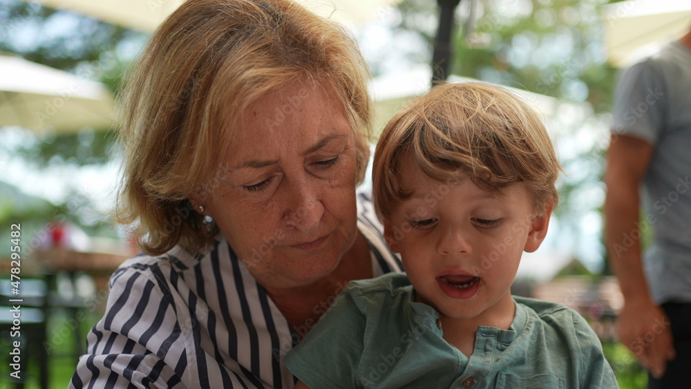 Grand-mother holding toddler grand-son in arms outside. candid and real life Grand-mother holding toddler grand-son in arms outside. candid and real life