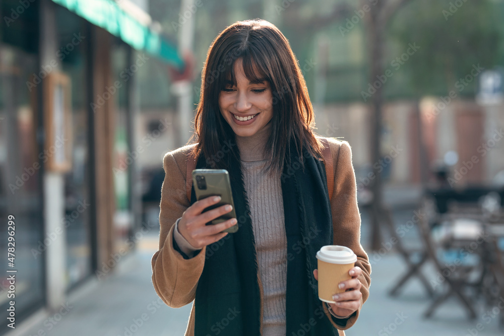 © nenetus - Pretty young woman using her mobile phone while drinking cup of coffee walking the streets of the city. © nenetus - Pretty young woman using her mobile phone while drinking cup of coffee walking the streets of the city.