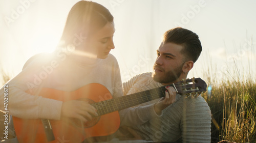Coppia di ragazza e ragazzo suona la chitarra seduti sul parco al tramonto photo