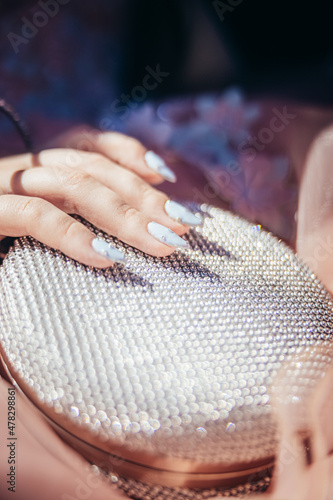 Girl with long nails holds a glittering white purse. Prom day. Girl has her first prom. High quality photo