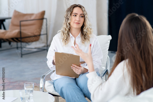 A female doctor listens to the patient problems, a clipboard in her hands. Professional psychological assistance. Doctor and the patient are sitting. Consultation of a psychotherapist