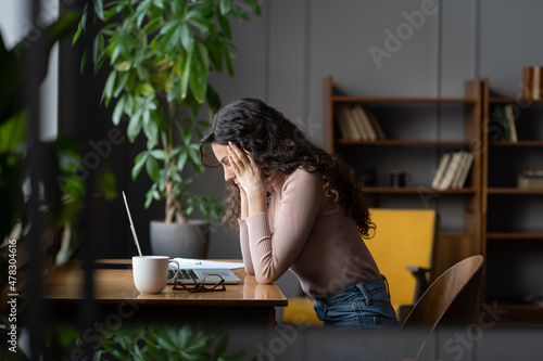 Young frustrated female employee getting stuck on task or project, sitting in front of laptop holding head in hands and thinking, tired account manager cant deal with deadline at work. Selective focus photo