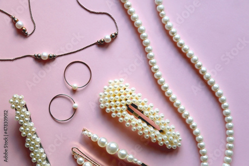Various pearl jewelry and hair accessories on pink background. Flat lay. 
