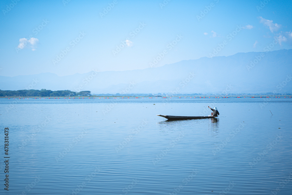 Fisherman is fishing on the wooden boat int the lake with mountain and blue sky background. Fisherman is fishing on the wooden boat int the lake with mountain and blue sky background.