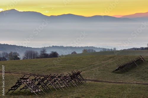 Mountain autumn landscape at dawn. With hay dryers in the foreground. Colored sky shortly before sunrise. Beautiful hills in the background. Protected area Vrsatec, Slovakia.