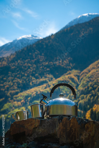 Close-up of a metal teapot and two cups on a stone against the background of mountains on a sunny day, copy the space. Beautiful, atmospheric autumn landscape of picnic mountains. Vertical photo photo