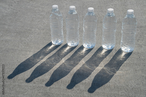 Five plastic water bottles stand in a row with long shadows photo
