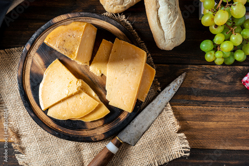 Aerial view of a piece of provolone cheese cut on a table and some grapes in the background. photo