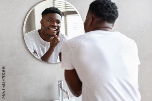 Black Guy Touching Unshaven Chin Smiling To Mirror In Bathroom