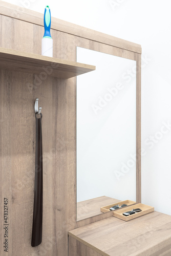 Wooden wall with a mirror, shoe horn hanging on a hanger and pet hair remover roller standing on a wooden board. Furniture next to entry door. Corridor equipment. photo