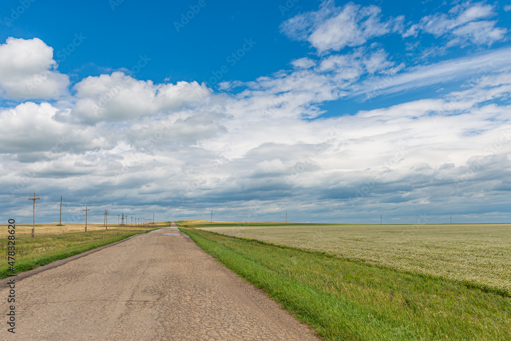 A wide road stretching into the distance and against the backdrop of endless fields and hills on a summer day. A wide road stretching into the distance and against the backdrop of endless fields and hills on a summer day.