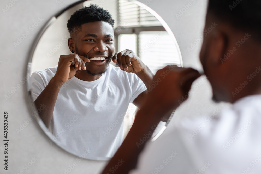 Black guy flossing teeth with tooth floss near mirror indoor - obrazy, fototapety, plakaty 