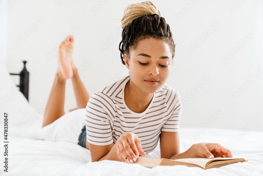 Young black woman reading book while lying on bed Young black woman reading book while lying on bed