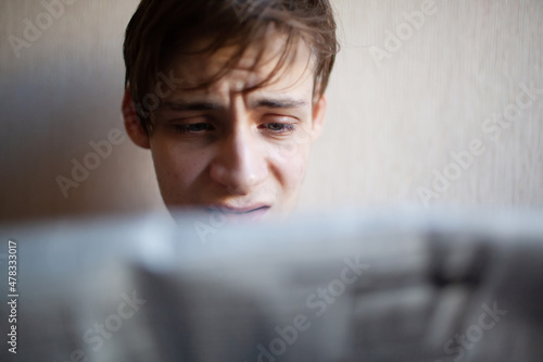 Young man reading a newspaper with emotions on his face