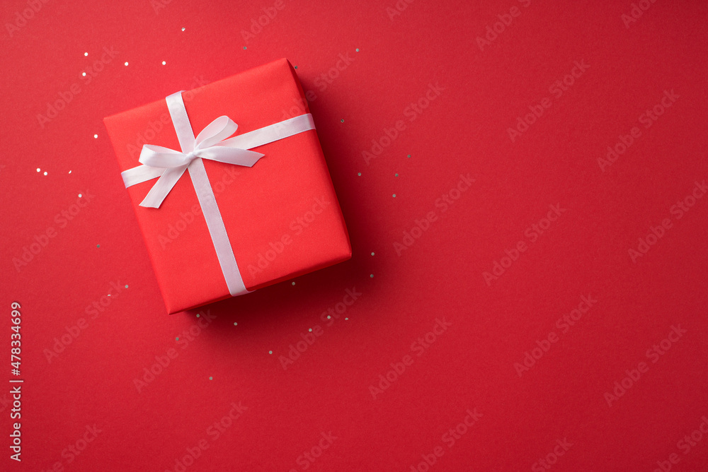 Top view photo of valentine's day decorations glowing sequins and red giftbox with white ribbon bow on isolated red background with copyspace Top view photo of valentine's day decorations glowing sequins and red giftbox with white ribbon bow on isolated red background with copyspace