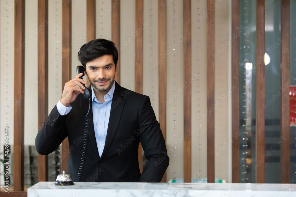 Handsome male receptionist is talking to a tourist who is making a online booking over the phone Handsome male receptionist is talking to a tourist who is making a online booking over the phone