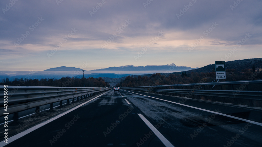 Highway at dawn car travels the road to the snow-capped mountains cold temperature, free road with no traffic