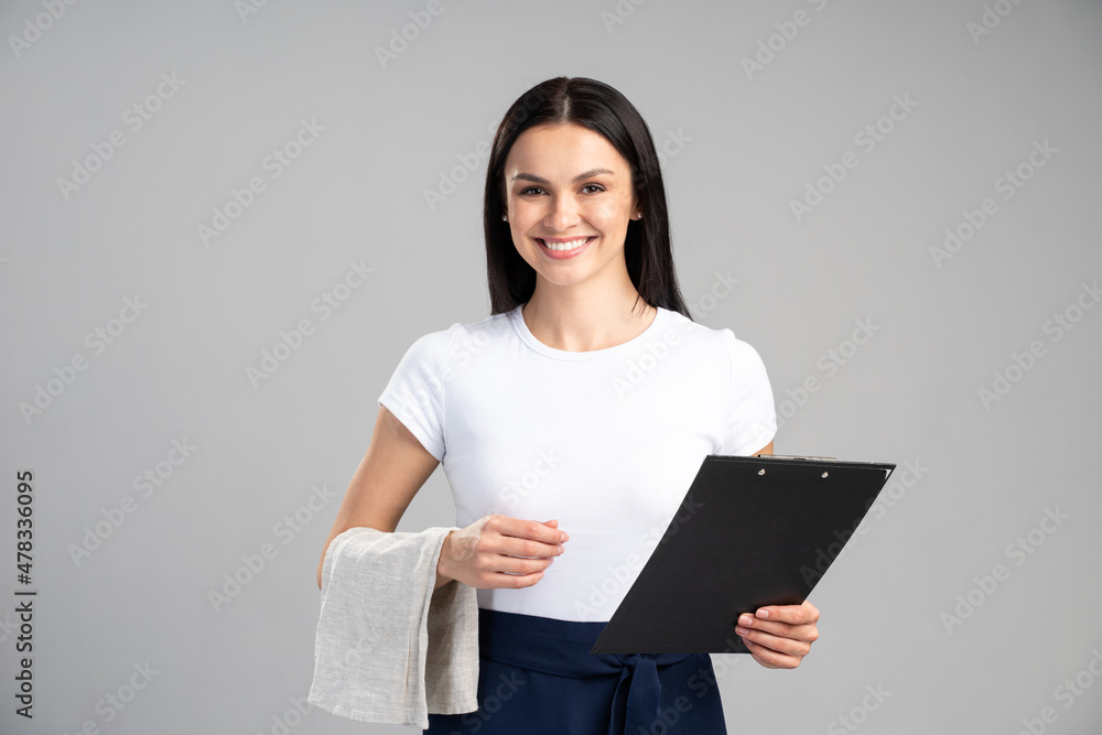 Waist up portrait view of the female waiter holding towel and folder with menu while posing on a grey background. Stock photo Waist up portrait view of the female waiter holding towel and folder with menu while posing on a grey background. Stock photo