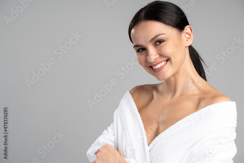 Portrait of young caucasian woman with beauty face and healthy hydrated facial skin standing in bathrobe with naked shoulder isolated on copy space background. Cosmetology  dermatology concept
