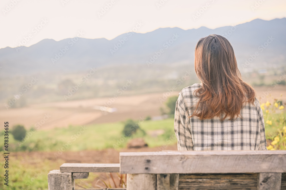 Rear iew point of young woman sitting on chair and looking to faraway with countryside environment Rear iew point of young woman sitting on chair and looking to faraway with countryside environment