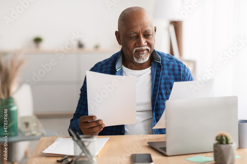 Senior African Businessman Working With Papers Sitting At Laptop Indoor