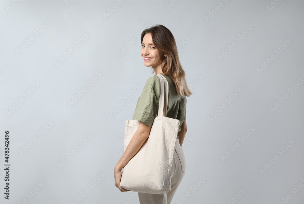 Happy young woman with blank eco friendly bag on light background Happy young woman with blank eco friendly bag on light background