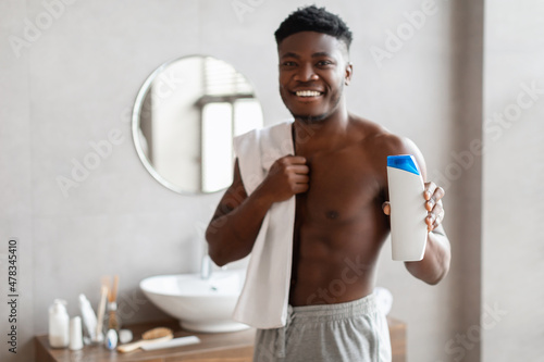 Cheerful African American Guy Showing Shower Gel Bottle In Bathroom