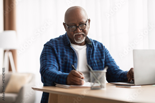 African American Man Taking Notes Sitting At Laptop In Office