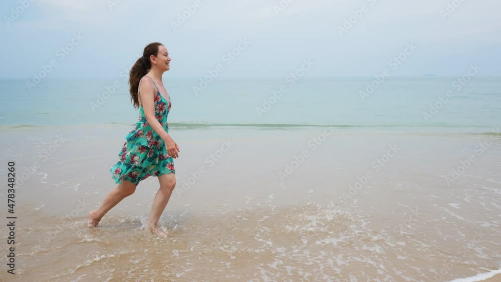 Cheerful lady walk at beach, enjoy vacation days at Thailand seaside. Uprush water splash on her steps, small waves break and curl with sand. Tracking camera move beside woman Cheerful lady walk at beach, enjoy vacation days at Thailand seaside. Uprush water splash on her steps, small waves break and curl with sand. Tracking camera move beside woman