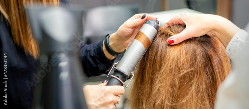 Hands of female hairstylist curls hair client with a curling iron in a hairdressing salon, close up