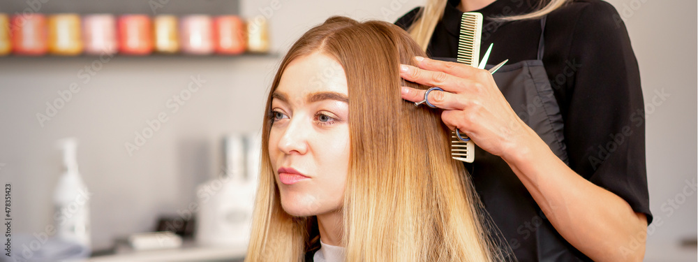 Fototapeta premium Gorgeous blonde long hair woman and her hairdresser looking and checking out hairstyle. Beautiful hairstyle of a young blonde woman after dying hair in a beauty salon, results of hair treatment