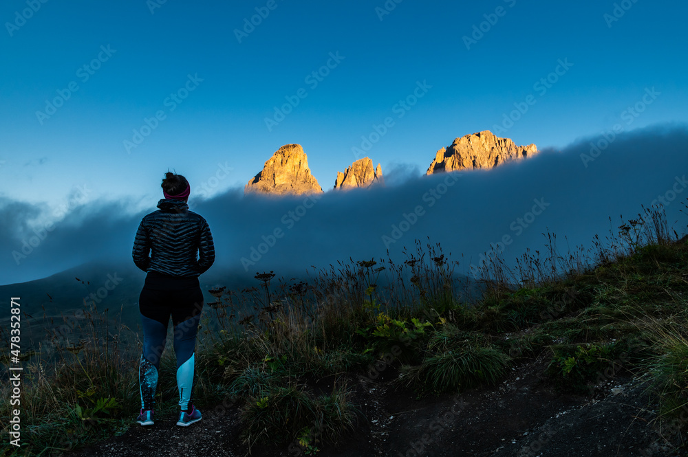 Young woman in sport clothes watching sunrise on mountain rock towers of Langkofel Group, Grohmannspitze mountain, Fuenffingerspitze mountain and Langkofel Mountain, Sella Pass, Dolomites, Alto Adige