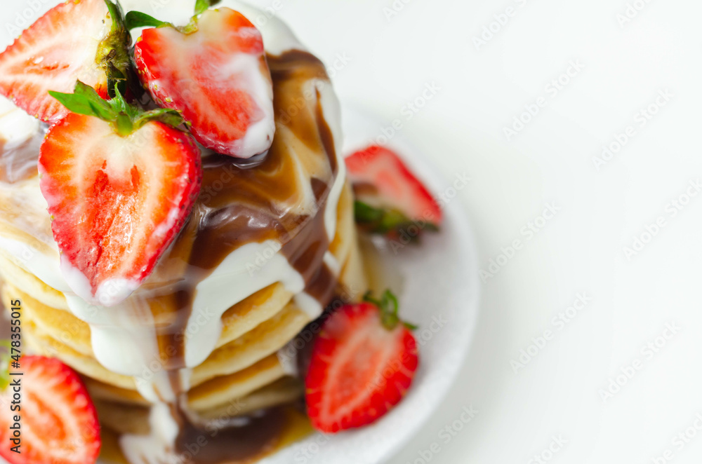 Pancakes stacked with strawberries, topped with  chocolate sauce and yoghurt