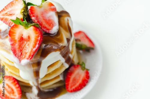 Pancakes stacked with strawberries, topped with chocolate sauce and yoghurt