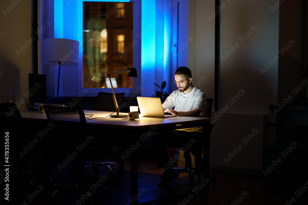 Freelancer guy student combining work and education study for exam or job interview at night in empty coworking center. Ambitious young businessman stay in office overtime busy with creative ideas Freelancer guy student combining work and education study for exam or job interview at night in empty coworking center. Ambitious young businessman stay in office overtime busy with creative ideas