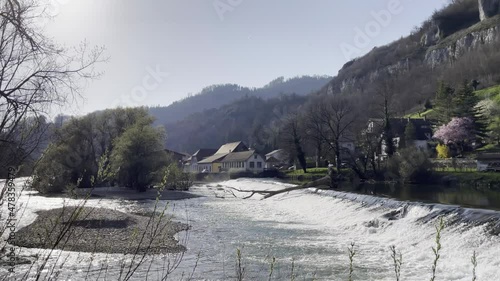 View of the Saint-Ursanne waterfalls with a fallen trunk, in the Doubs river in a park