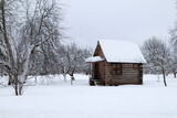 snow covered old brown wooden house in the winter field